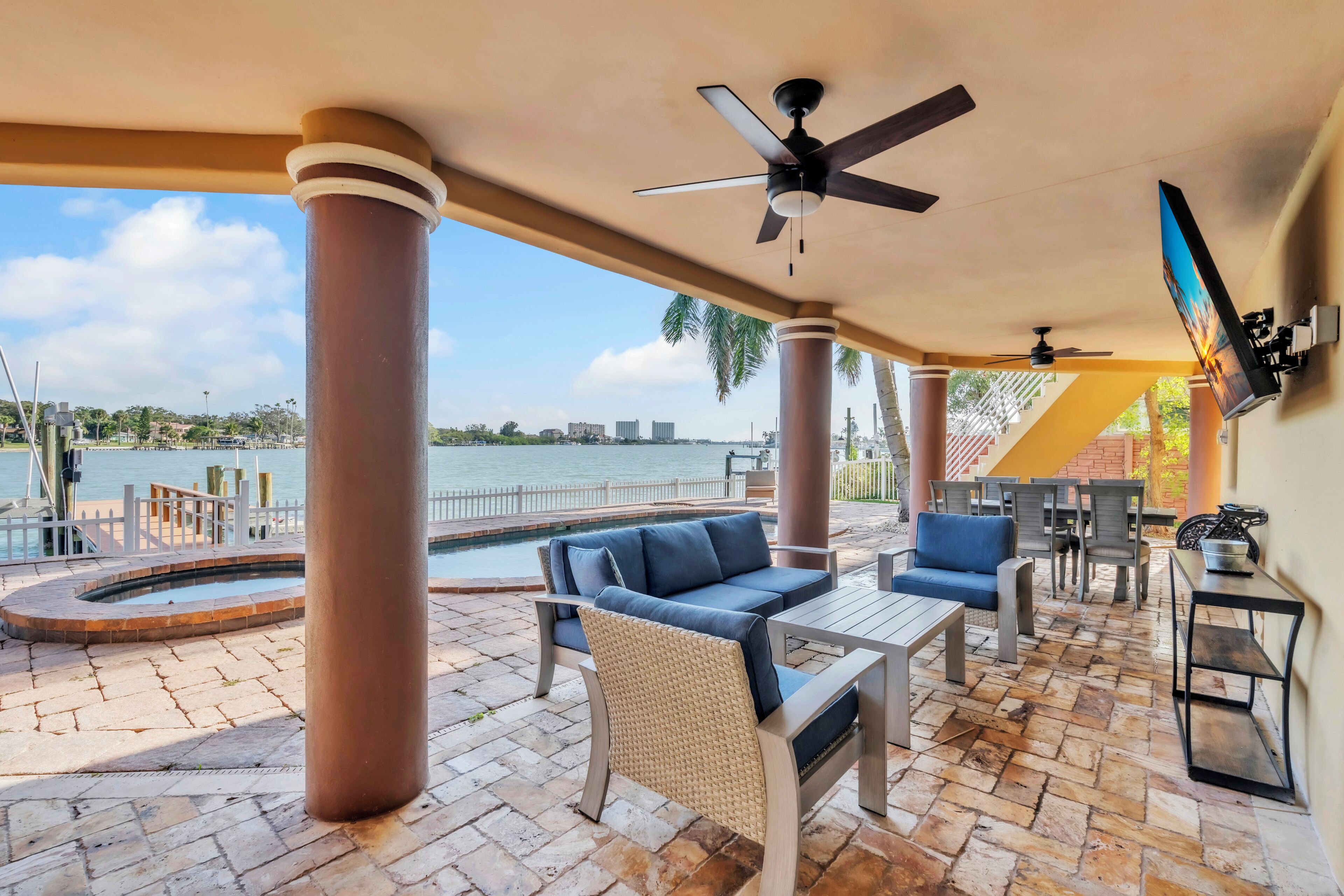 An outdoor patio with a pool, seating, and a TV mounted on the wall.