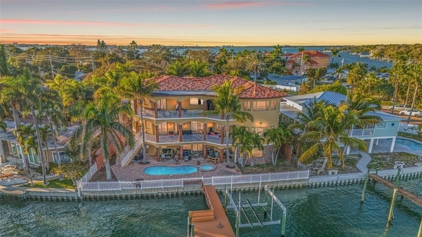 A large, multi-story house with a pool, surrounded by palm trees and a dock.