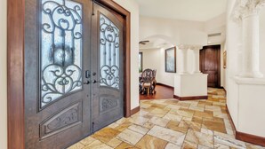 A hallway with a herringbone patterned floor, a wooden door with decorative glass panels, and a white column with intricate detailing.