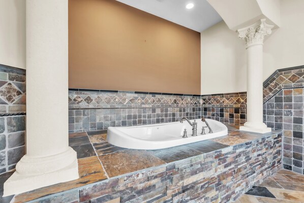 A bathroom with a freestanding bathtub, mosaic tile backsplash, and white columns.