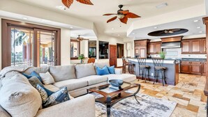 A spacious living room with a large sofa, a coffee table, and a kitchen area with wooden cabinets and a bar.