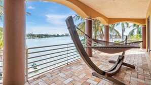 A hammock under a curved roof, overlooking a body of water with palm trees and a distant cityscape.