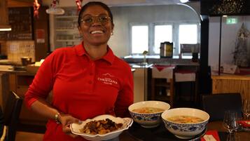 A person in a red shirt holding a plate with food and two bowls of soup on a table.
