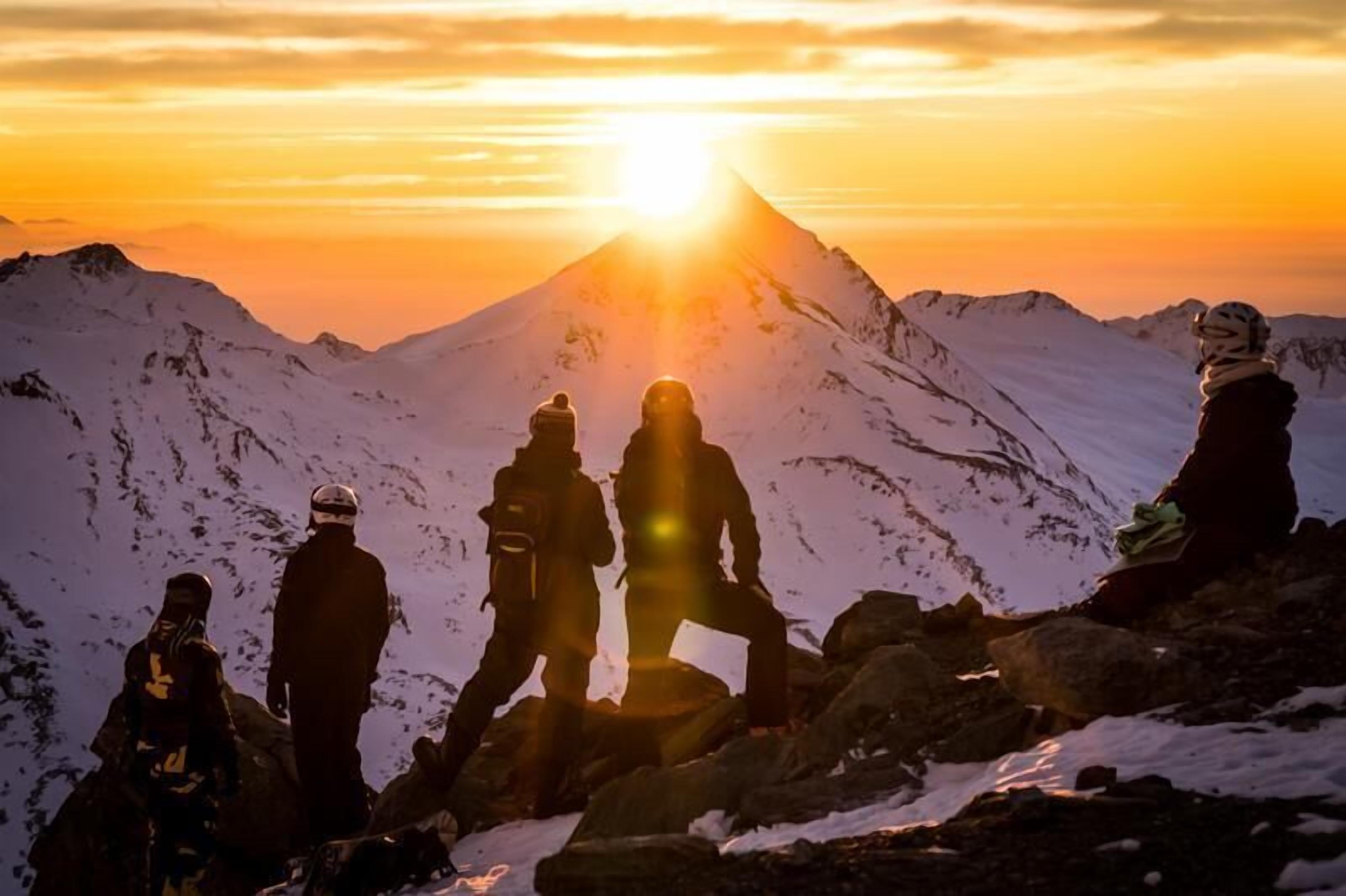 A group of people on a mountain peak with a sunset in the background.