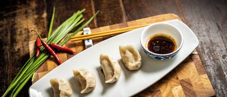 A plate of dumplings with a dipping sauce on a wooden board.