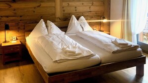 Ένα  διπλό κρεβάτι με λευκά σεντόνια, ένα ξύλινο προσκέφαλο, ένα κομοδίνο με ένα φωτιστικό και ένα παράθυρο με κουρτίνες.