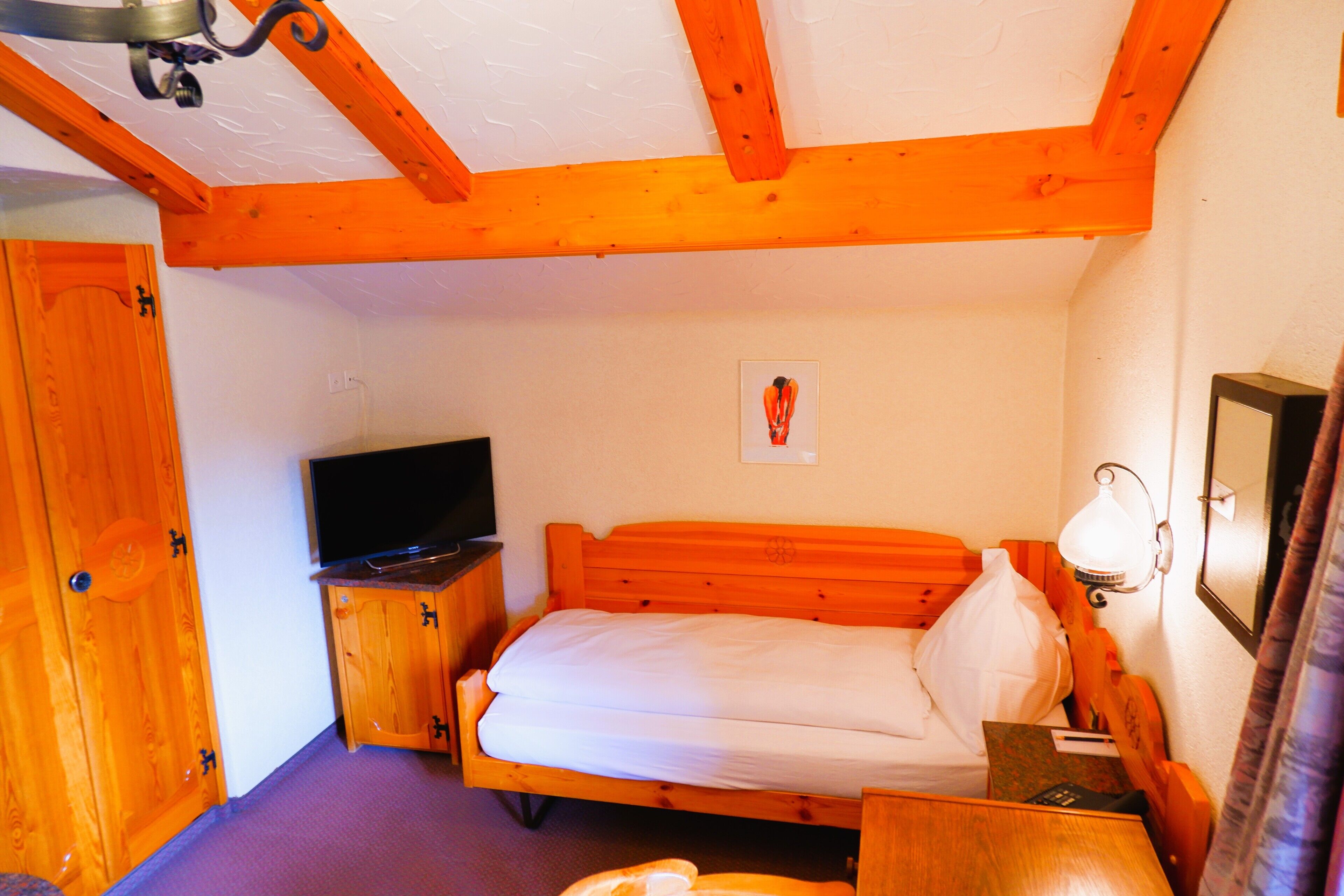 A bedroom with a wooden bed, a television on a wooden stand, and a wall-mounted light fixture.