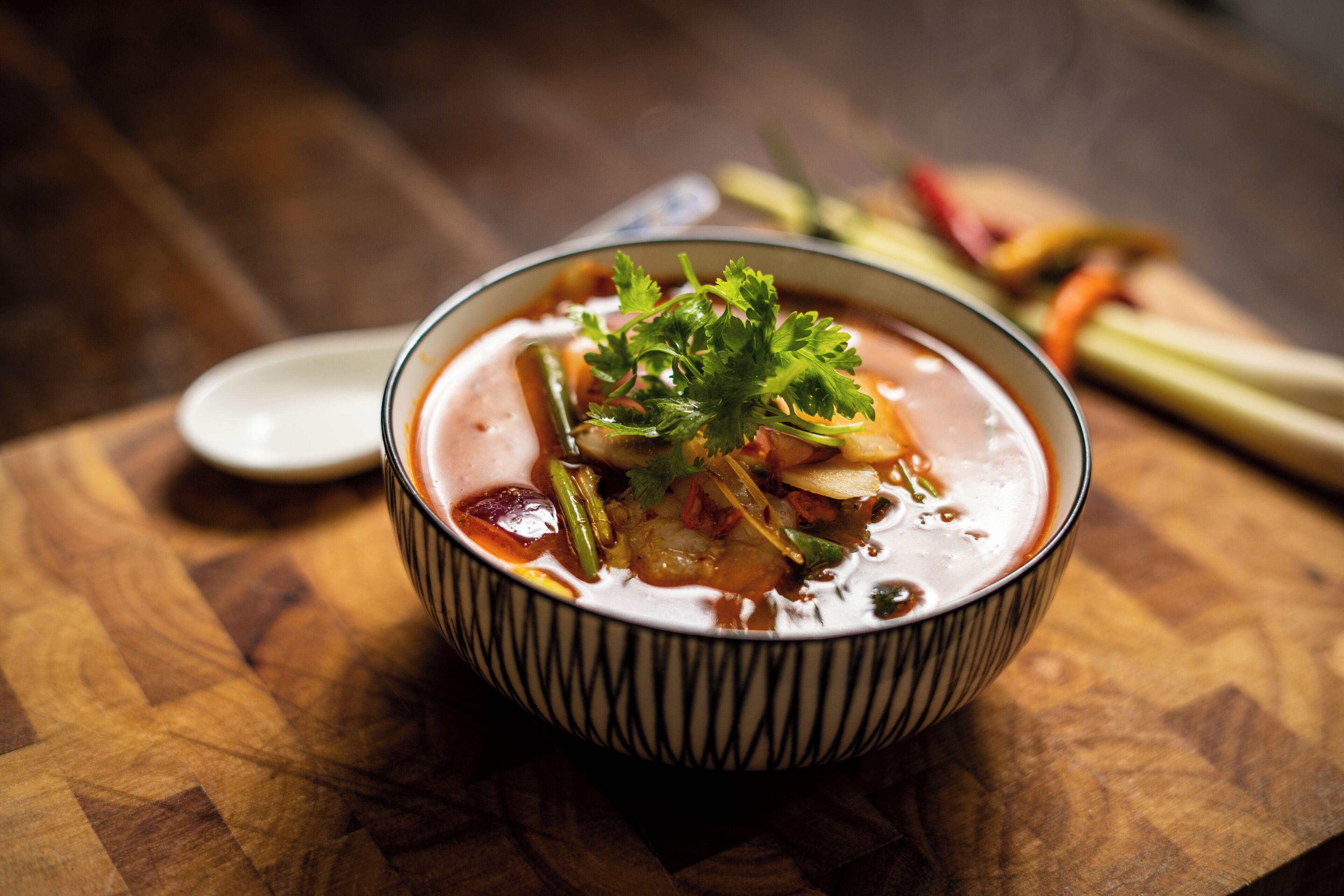 A bowl of soup with vegetables and a garnish on a wooden table.