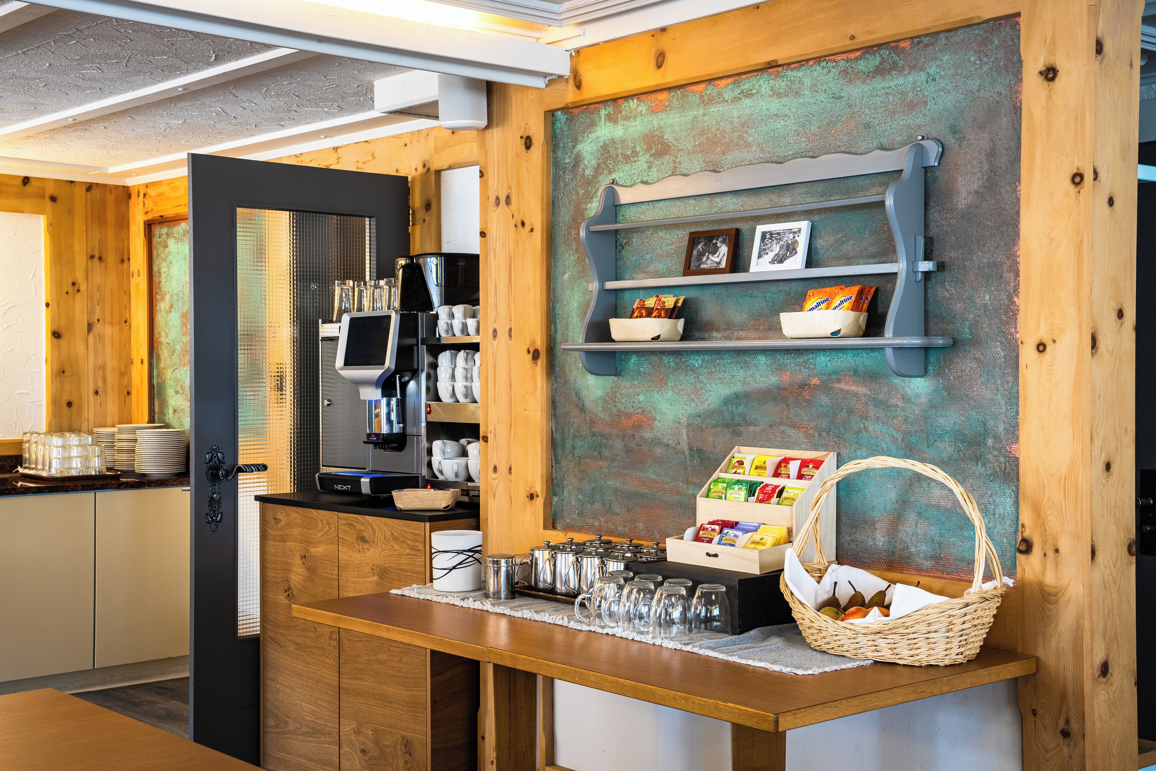 Een keukenhoek met een koffieapparaat, planken met etenswaren en een mand met fruit.
