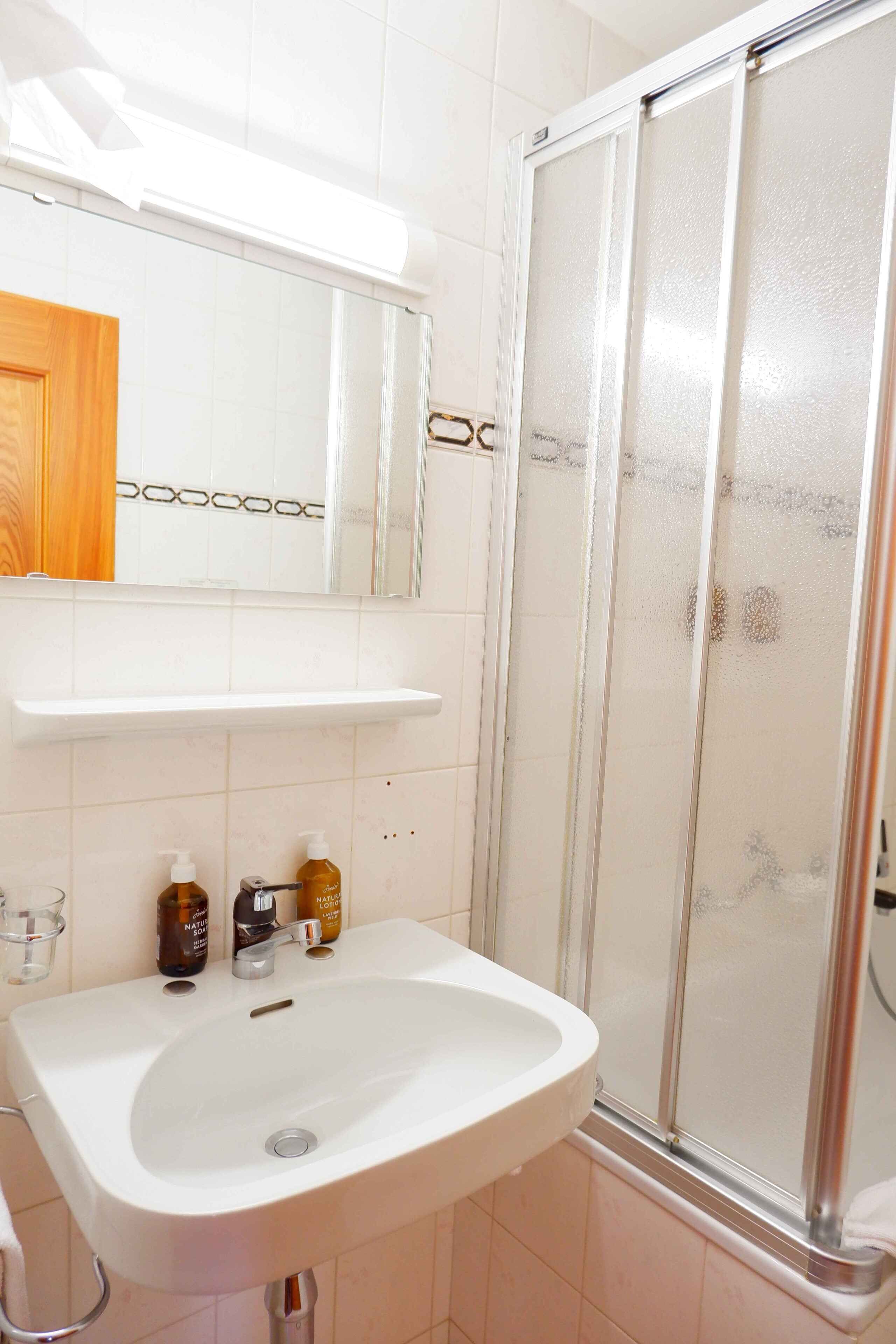 Un baño con lavamanos blanco, espejo y cabina de ducha.