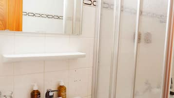 Un baño con lavamanos blanco, espejo y cabina de ducha.