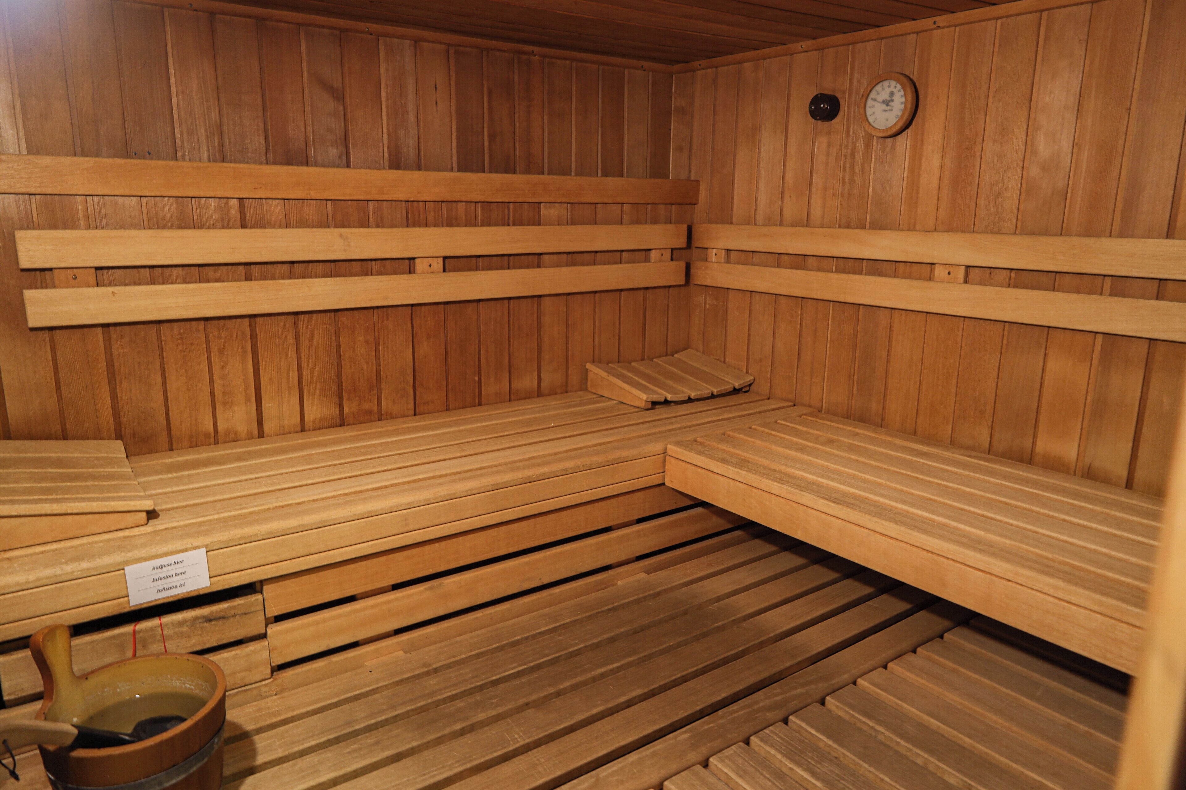 A wooden sauna with benches and a small table with a bowl and ladle.