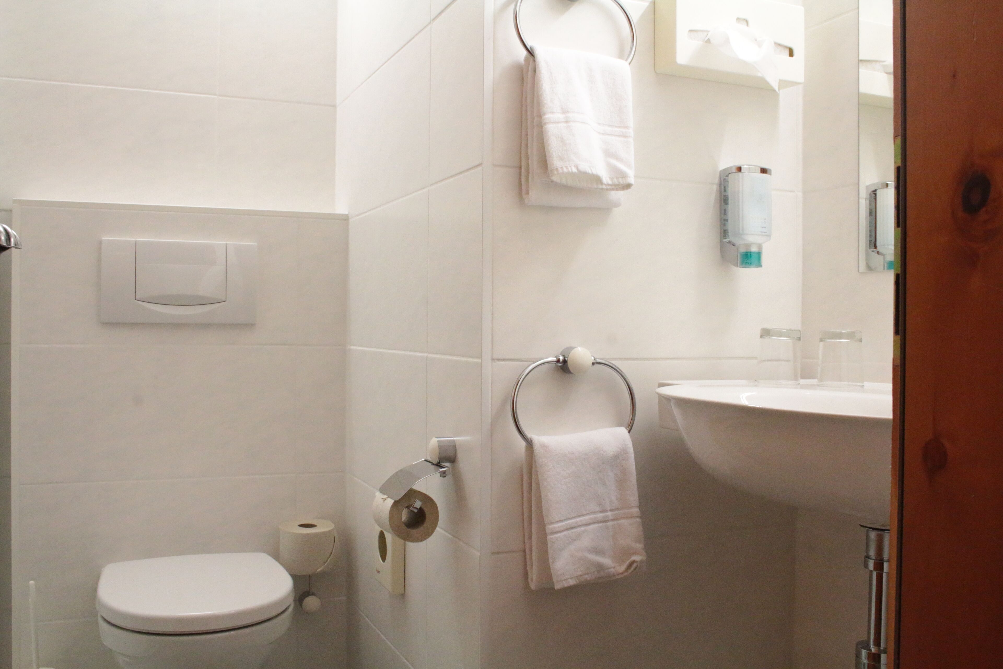 A bathroom with a toilet, toilet paper, a towel rack with towels, and a sink with a mirror.