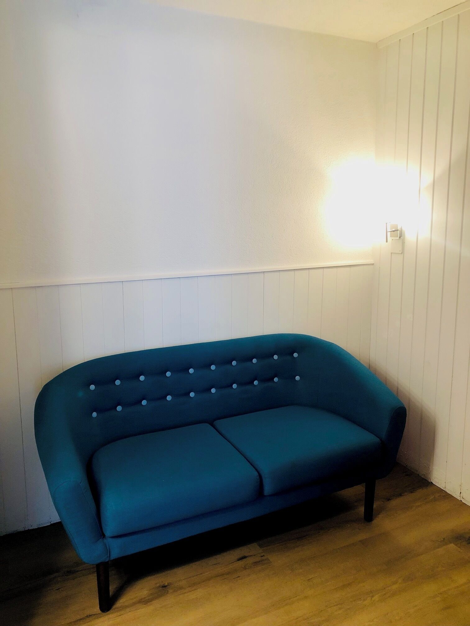 A teal sofa against a white wall with a light fixture.