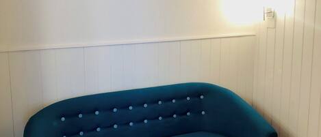 A teal sofa against a white wall with a light fixture.