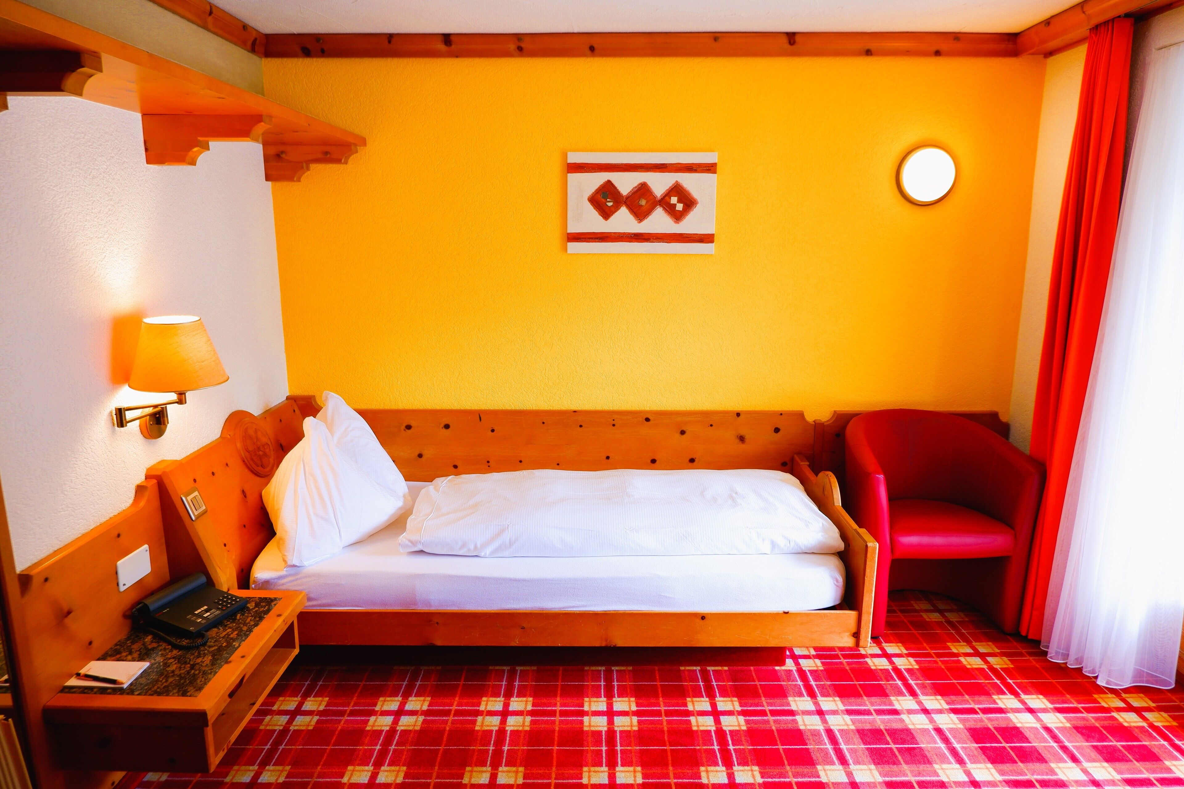 A room with a wooden bed, a red chair, a lamp, and a wall-mounted artwork.