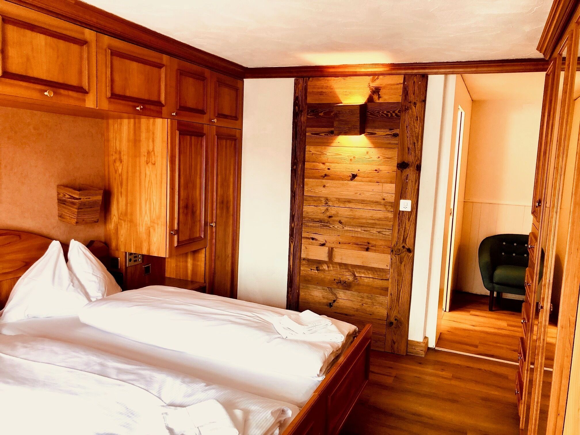 A bedroom with a wooden bed, a stone wall, and a green chair.