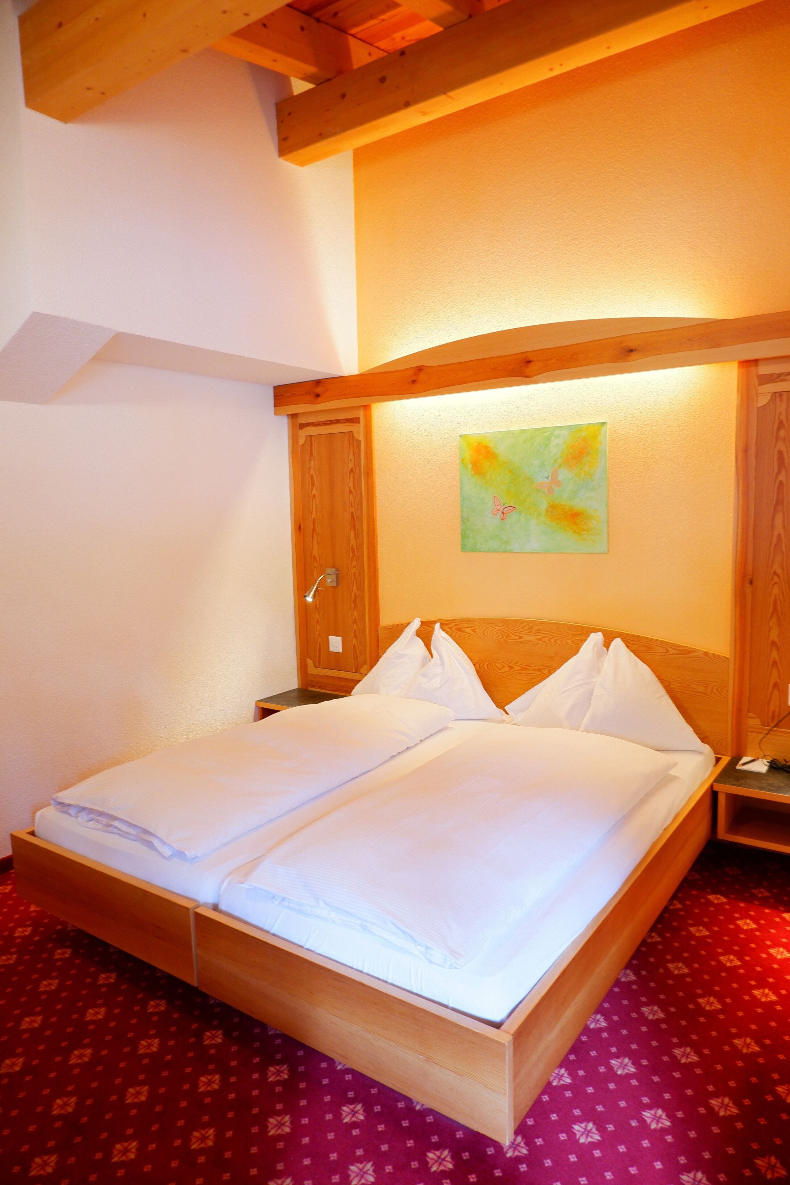 A neatly made bed in a room with wooden beams and a painting on the wall.