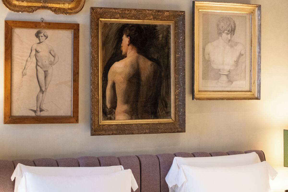 A bedroom with a bed, white pillows, and six framed artworks on the wall.