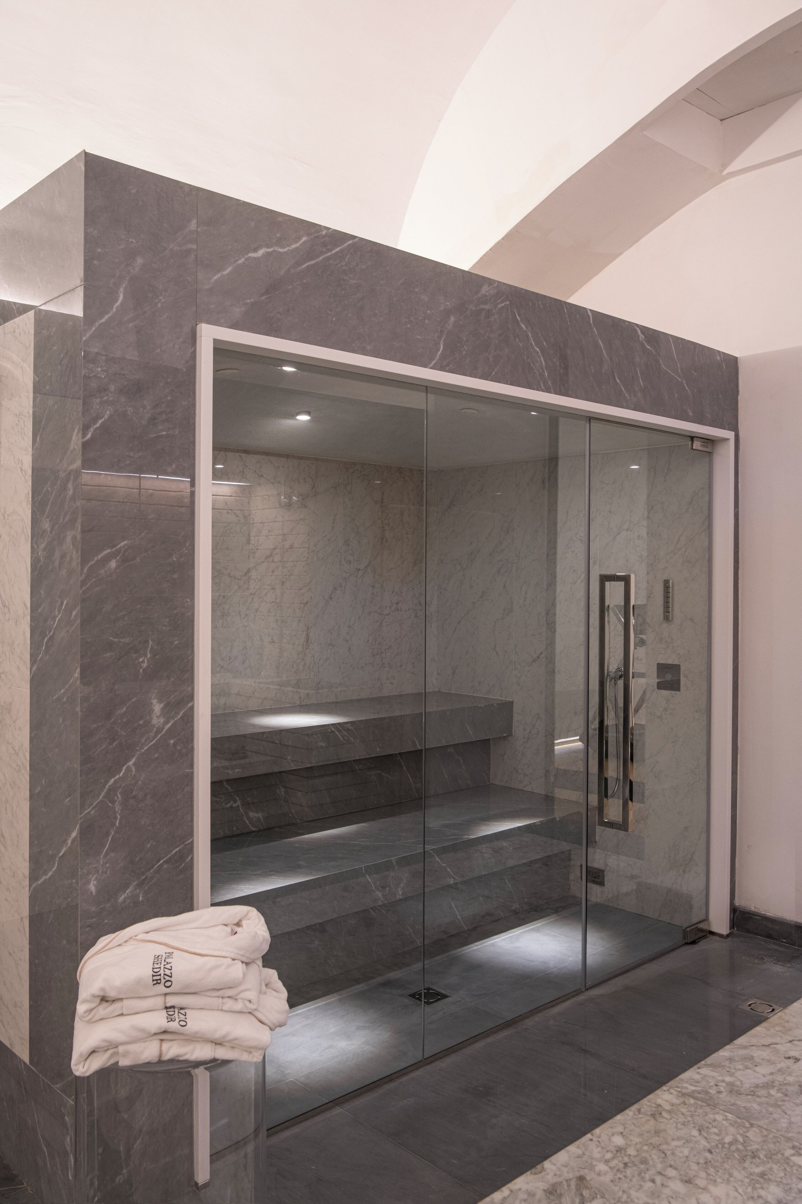 Un baño moderno con ducha de vidrio, paredes de mármol y una pila de toallas.