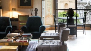 A spacious room with a high arched ceiling, a large window offering a view of a courtyard, and a seating area with multiple chairs and a table. - Palazzo Shedir - The Leading Hotels of the World (Rome)