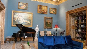 A grand room with a grand piano, a blue velvet sofa, and classical paintings on the walls. - Palazzo Shedir - The Leading Hotels of the World (Rome)