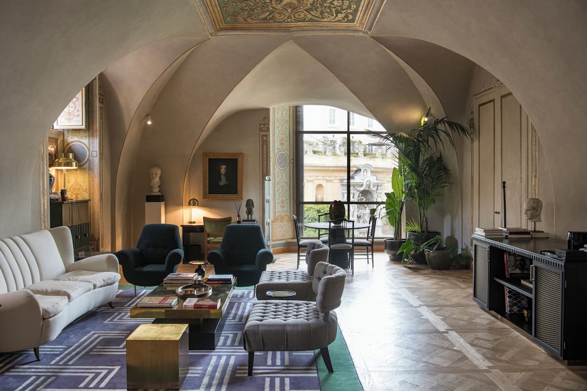 A spacious living room with a high arched ceiling, a white sofa, two armchairs, a coffee table, and a bookshelf.