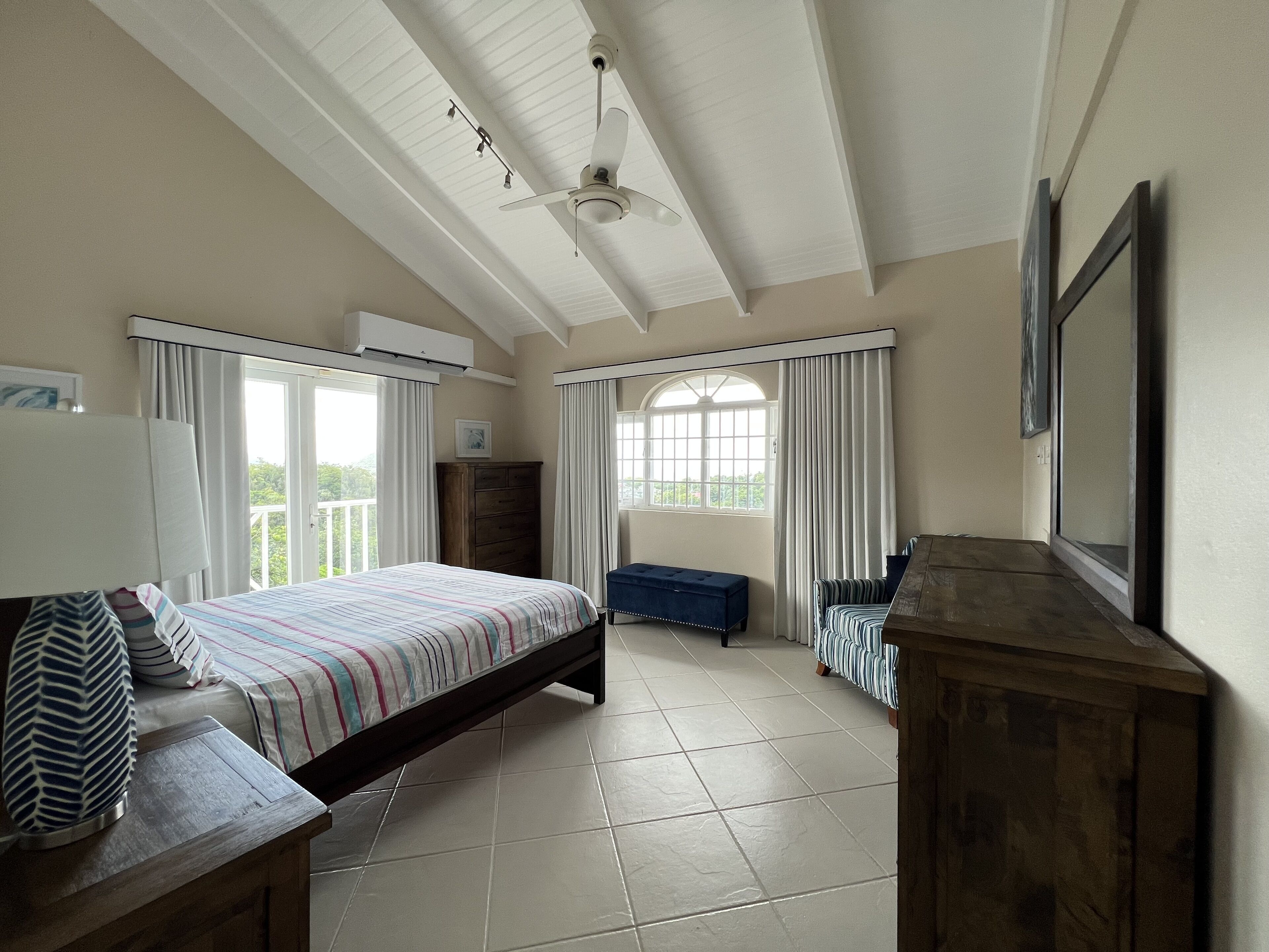 A bedroom with a bed, a wooden bench, a dresser, and a ceiling fan.