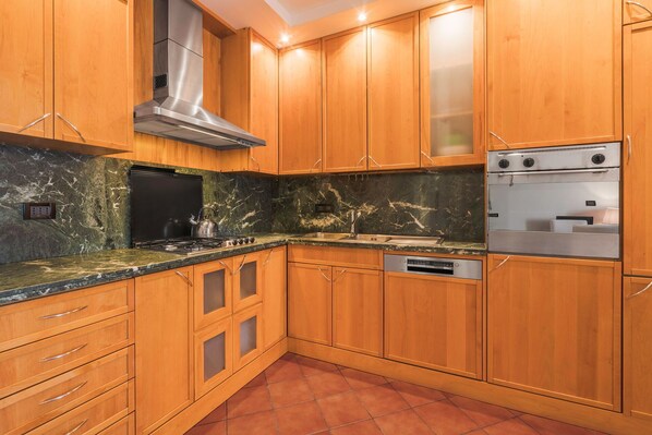 A kitchen with wooden cabinets, a stainless steel range hood, a built-in oven, and a marble countertop.