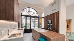 Une cuisine moderne dotée d’un grand îlot central, d’appareils électroménagers intégrés et offrant une vue dégagée grâce à une grande fenêtre.