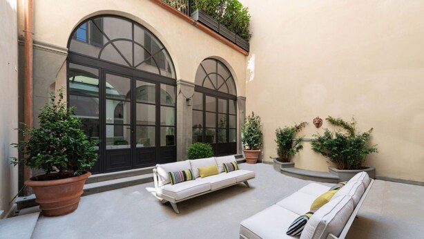 Une cour avec un canapé blanc, un fauteuil et des plantes en pot.