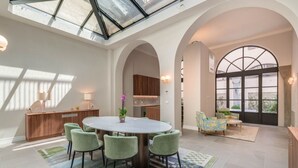Un vaste espace dédié à la salle à manger, avec une table ronde et des chaises vertes, un buffet en bois et une grande fenêtre offrant une vue dégagée.