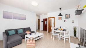 Uma sala de estar moderna com um sofá cinzento, uma mesa de centro branca e um espaço de jantar com uma mesa e cadeiras brancas.