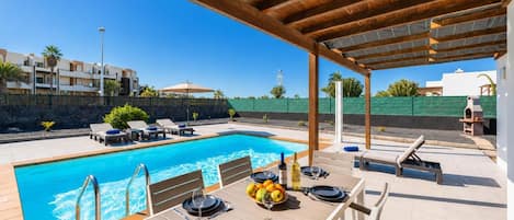 Zona de piscina amb una zona de seients coberta, una taula de menjador preparada per a dues persones i vista a la piscina.