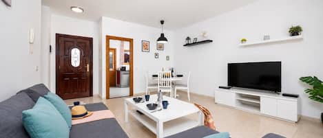 A living room with a sofa, coffee table, TV, and a dining area with chairs and a table.