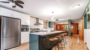 Una cocina moderna con una isla grande, electrodomésticos de acero inoxidable, taburetes de bar de madera y un ventilador de techo.