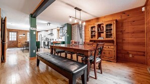 Un comedor amplio con una mesa y sillas de madera, un banco y una cocina al fondo.