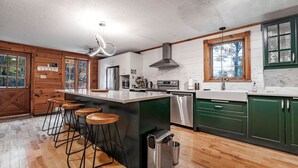 Una cocina moderna con una isla central, taburetes de bar, electrodomésticos de acero inoxidable y armarios verdes.