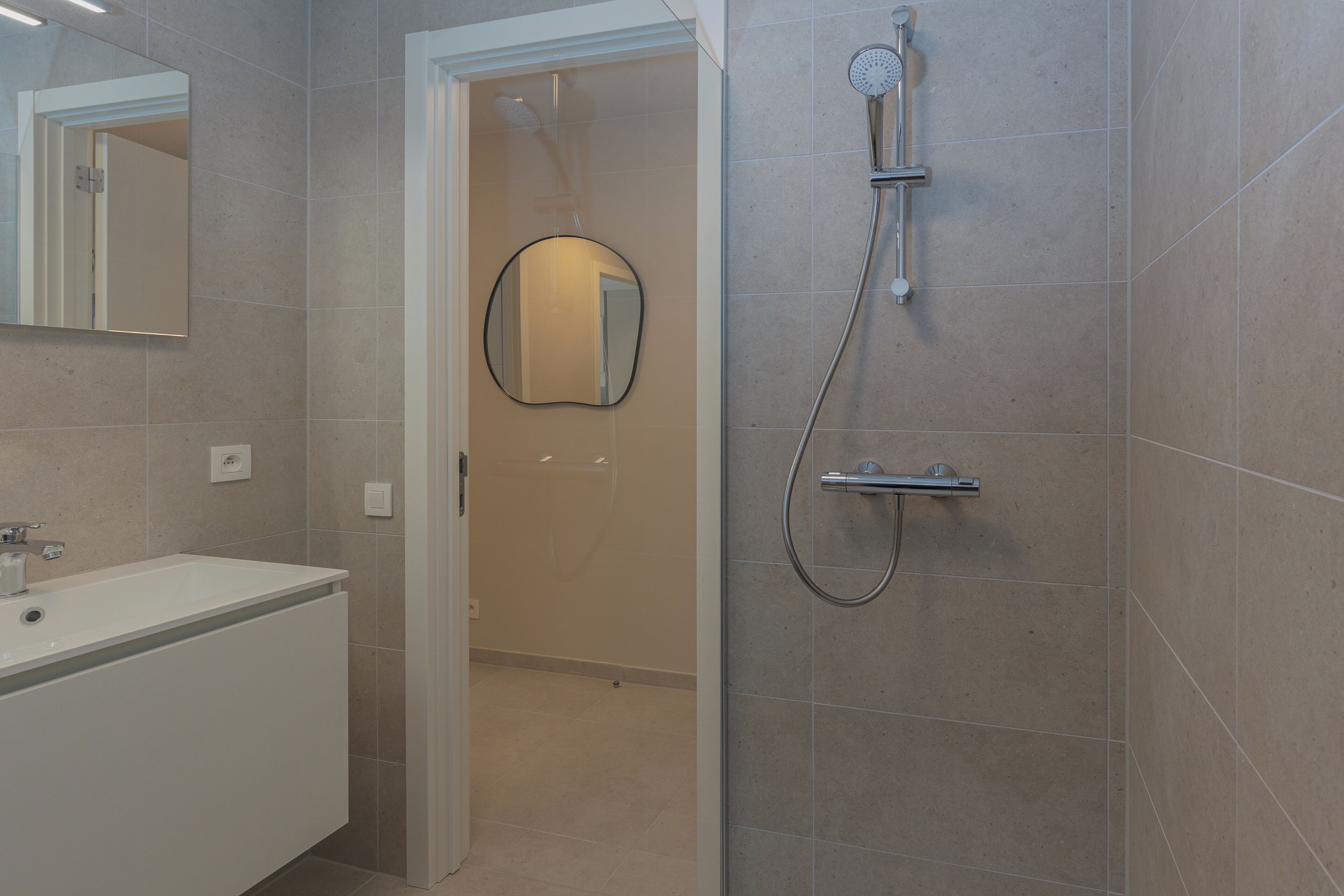 Un bagno moderno con un lavandino bianco, uno specchio e una doccia con soffione a mano.