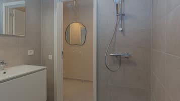Un bagno moderno con un lavandino bianco, uno specchio e una doccia con soffione a mano.