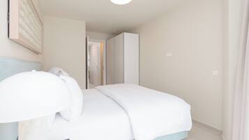 A bedroom with a bed, a bedside table, a lamp, and a door leading to another room.