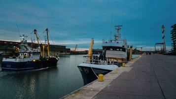 A harbor with a large ship docked at a pier, a smaller boat, and a building with a crane.