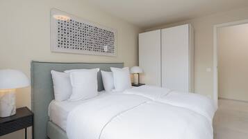 A neatly made bed with white bedding, a grey headboard, and a wall-mounted artwork.
