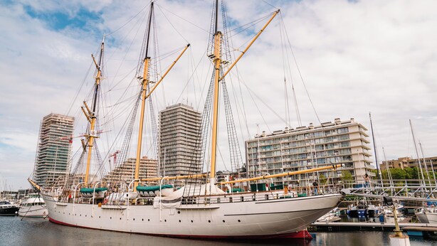 Ein großes Segelschiff liegt in einer Marina vor einer Gebäudereihe festgemacht.