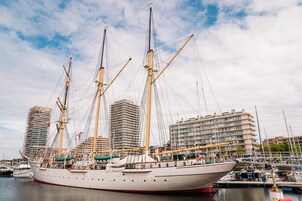Um grande navio a vela atracado em uma marina, com edifícios ao fundo.