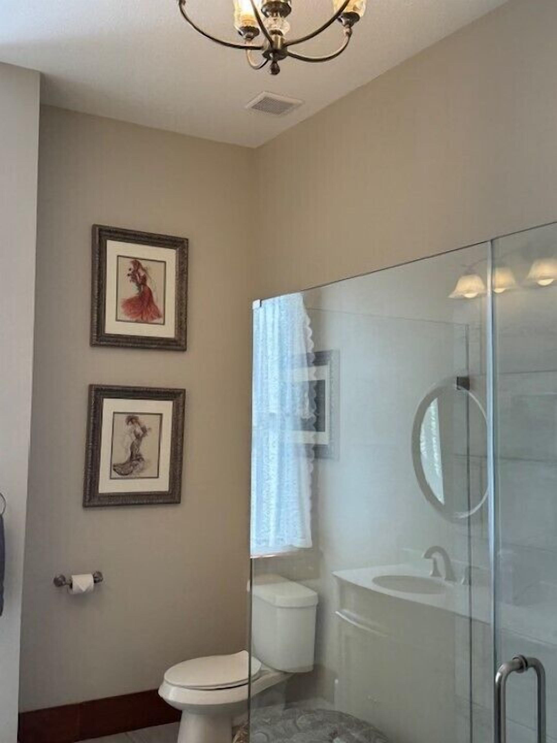 A bathroom with a glass-enclosed shower, a toilet, and framed artwork on the wall.