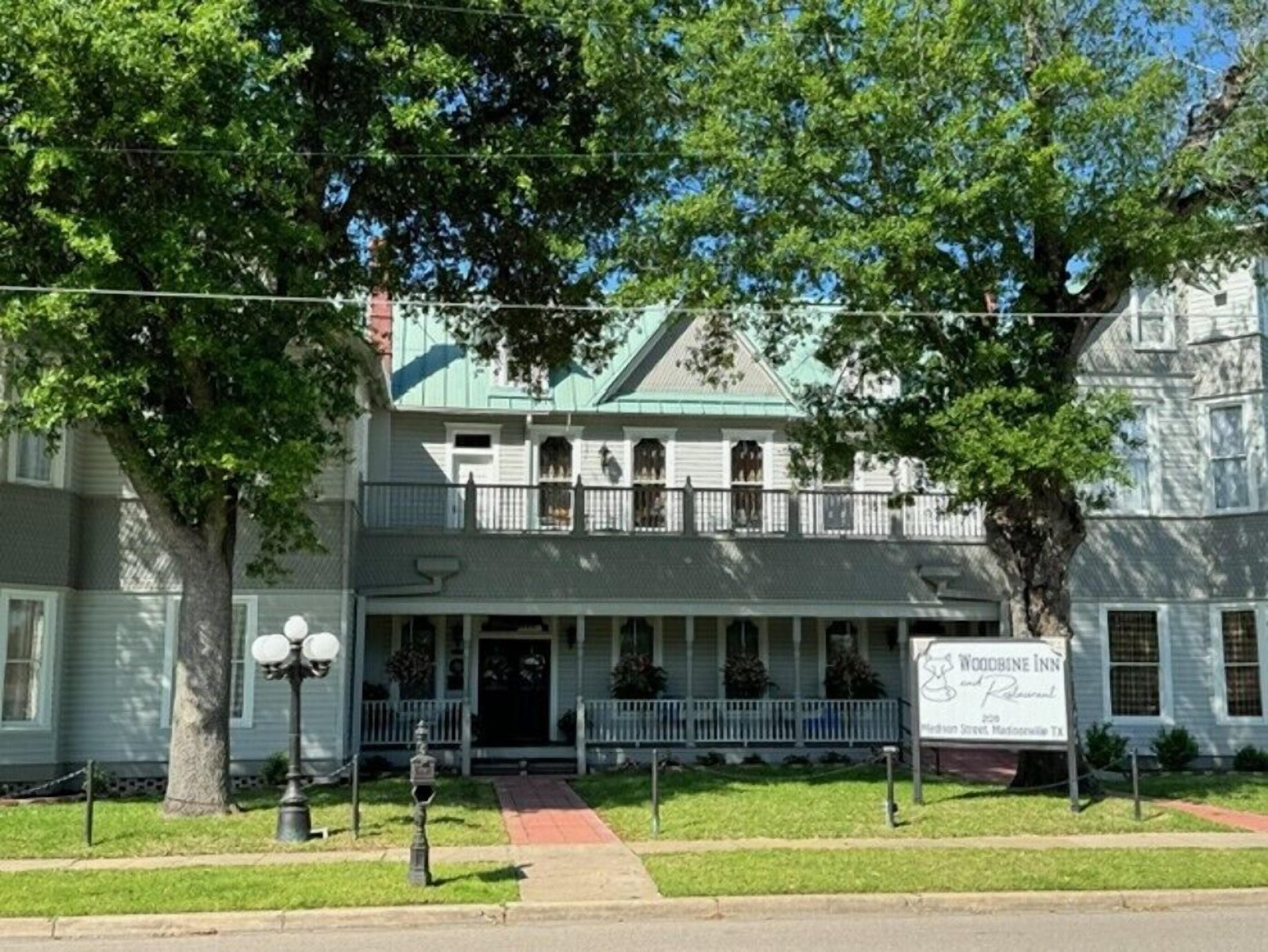 A two-story building with a green roof, a porch with railings, and a sign for Woodbine Inn.
