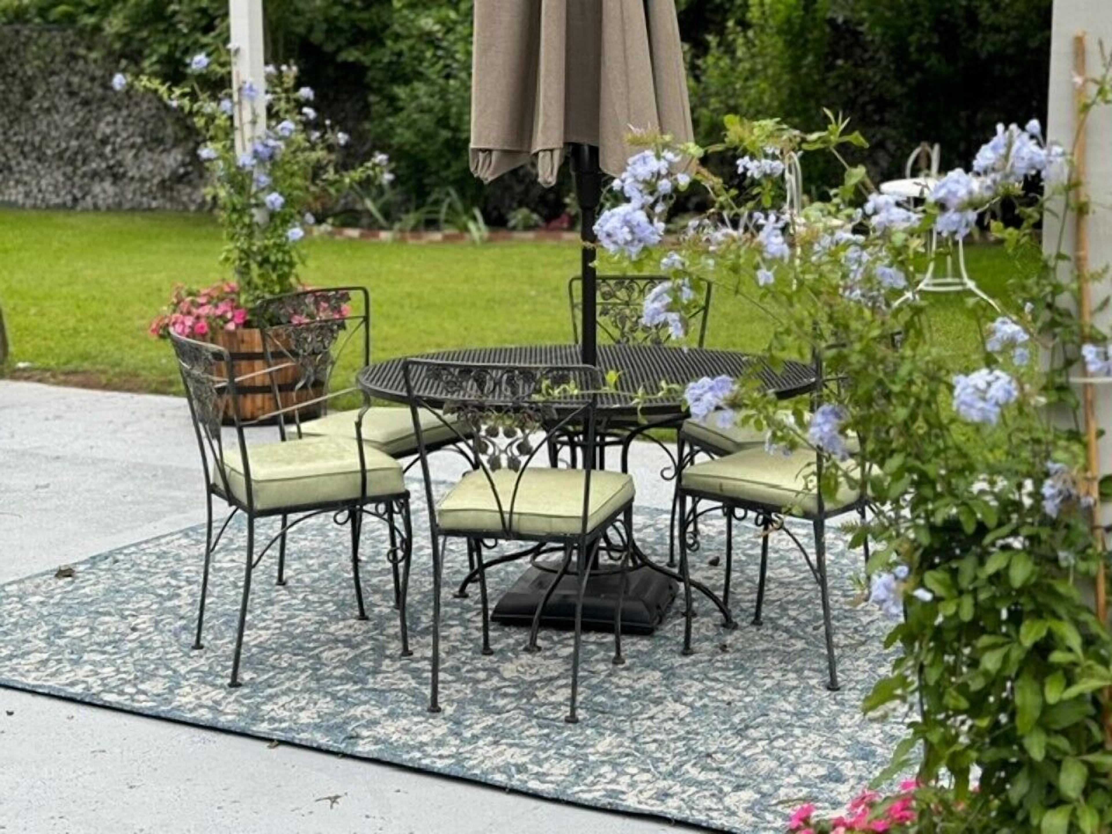 An outdoor patio with a round table and chairs, surrounded by a patterned rug.