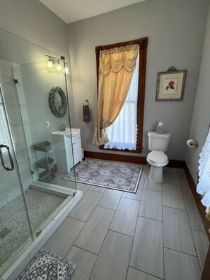 A bathroom with a glass shower enclosure, a toilet, and a sink.