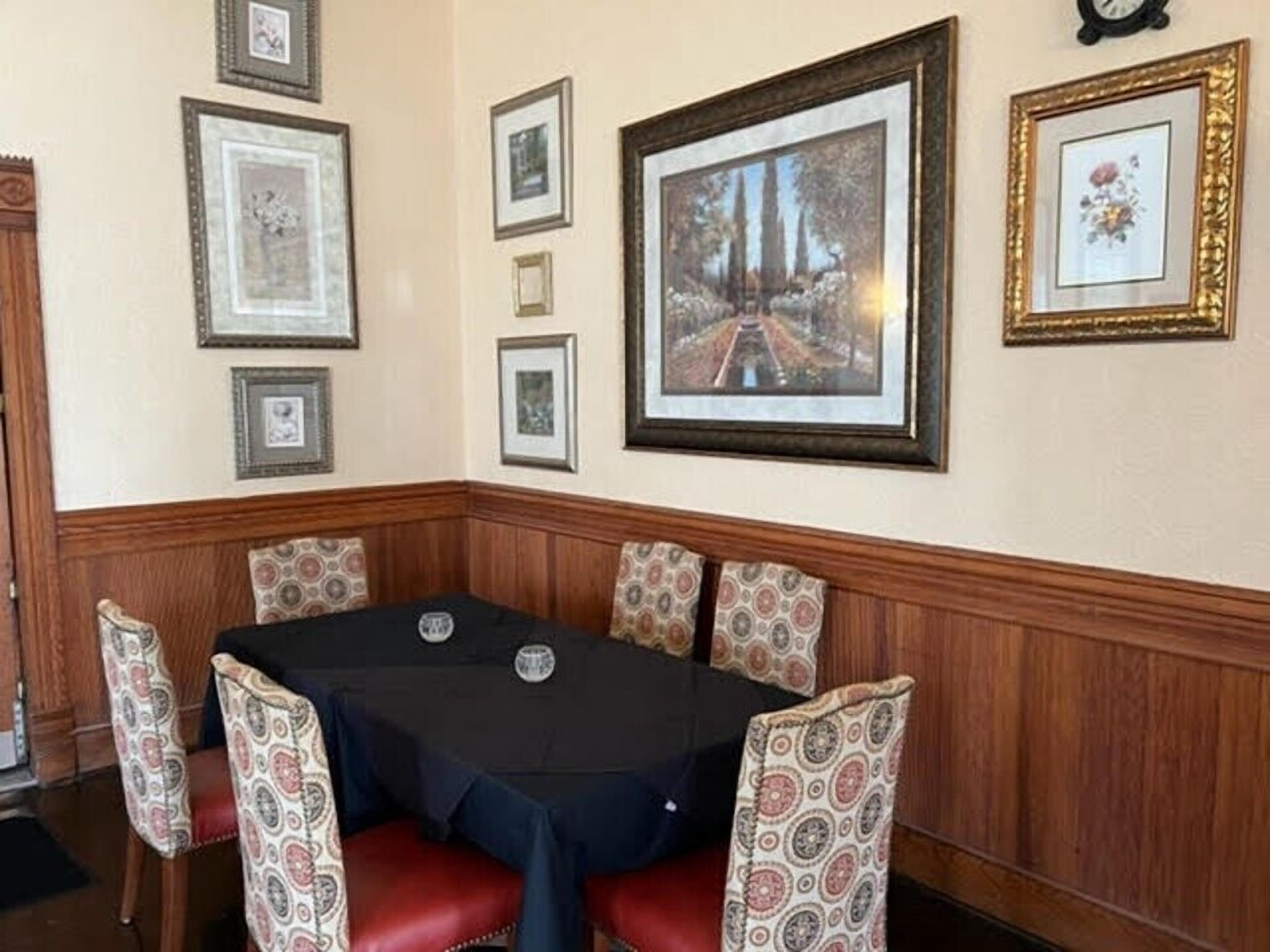 A corner dining area with a table and chairs, framed pictures on the wall, and a wooden panel design.